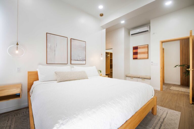 Bright, modern bedroom with white bedding, wooden furniture, and artwork on white walls in a residential property in Roatan, Honduras.