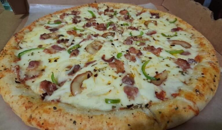 A freshly baked pizza topped with bacon, green peppers, mushrooms, and melted cheese on a wooden table in Roatan, Honduras.
