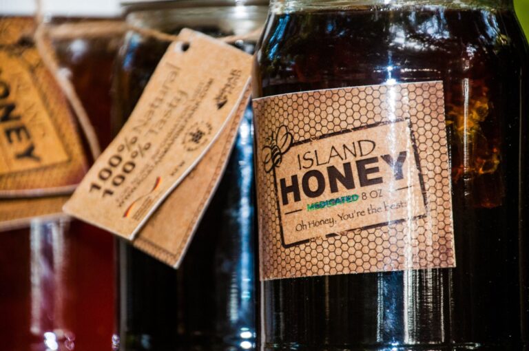 A dark amber jar labeled 'Island Honey' with a honeybee illustration, alongside other honey jars on a display shelf in Roatan, Honduras.