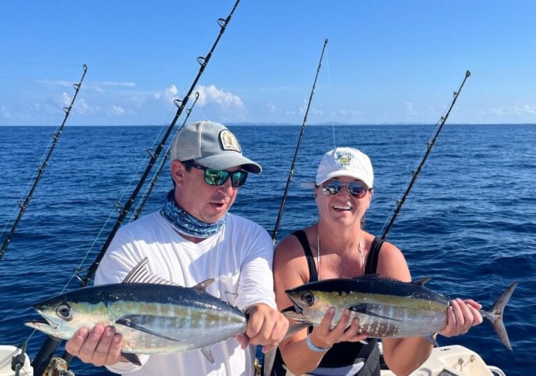 Two anglers hold freshly caught tuna aboard a boat in the ocean near Roatan, Honduras.