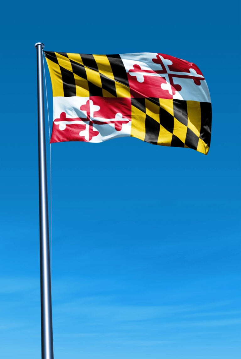 The image shows the Maryland state flag flying on a pole against a clear blue sky.