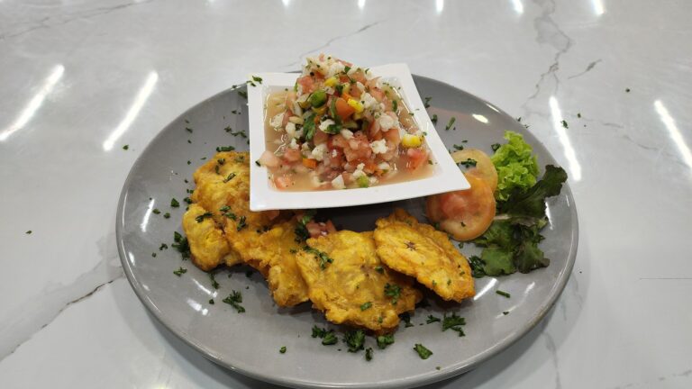 A plate of Honduran cuisine on a marble countertop features fried fish fillets, a side of fresh tomato and lettuce garnish, and a small bowl of ceviche topped with chopped vegetables and herbs, with "Roatan" visible in the context of a business listing.