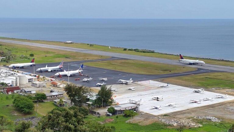 An aerial view of Roatan’s airport in Honduras showing multiple commercial airplanes parked on the tarmac, a runway extending toward the ocean, and a scenic coastline with the Caribbean Sea in the background.