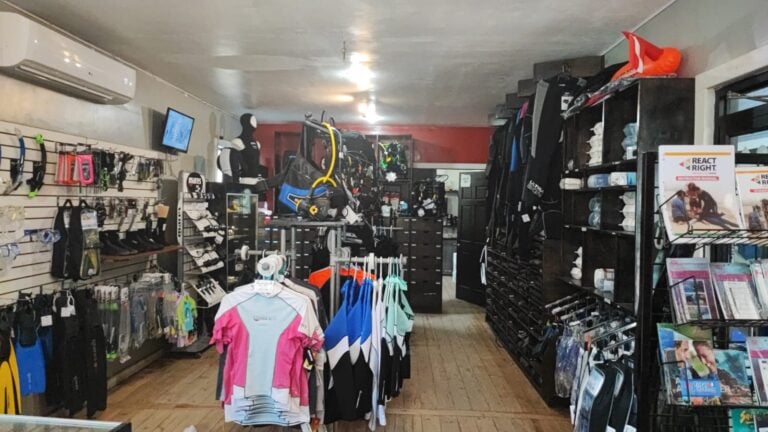 A retail store in Roatan, Honduras, displaying outdoor and sports equipment, including cycling gear, apparel, and accessories, with shelves and racks filled with helmets, clothing, and promotional materials.