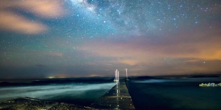 A starry night sky with the Milky Way over the ocean and a wooden pier extending into the water on Roatan, Honduras.