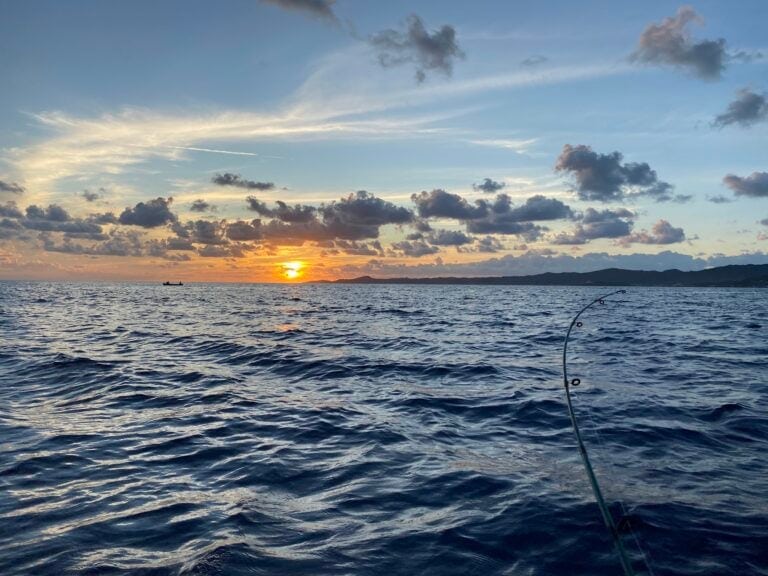 A boat sails on the ocean near Roatan in Honduras during a vibrant sunset with colorful clouds and distant landforms.