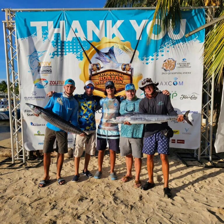 A group of five men holding large fish and posing in front of a banner at the XIV Annual Roatan International Fishing Tournament on Roatan, Honduras.