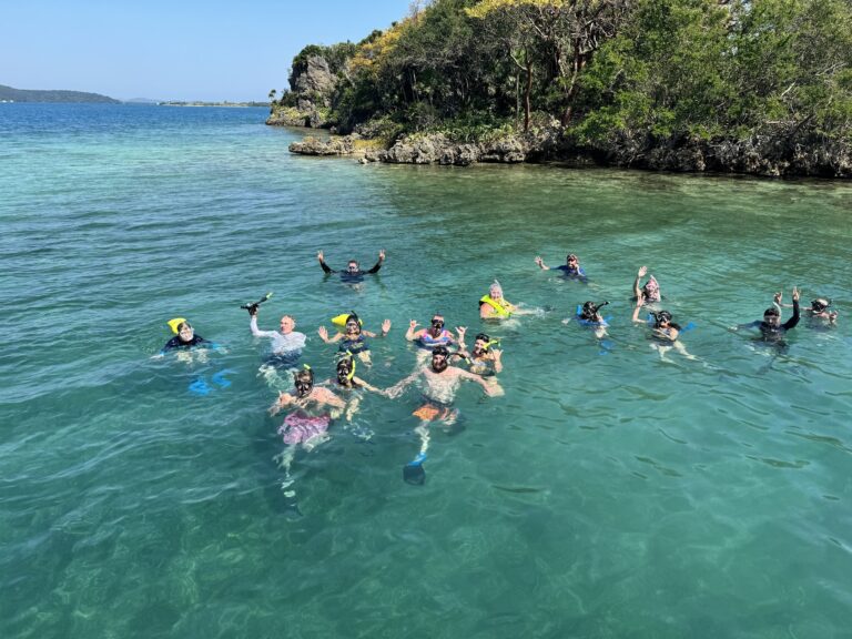 People snorkeling in clear turquoise waters near a rocky and forested coastline on Roatan in the Bay Islands of Honduras.