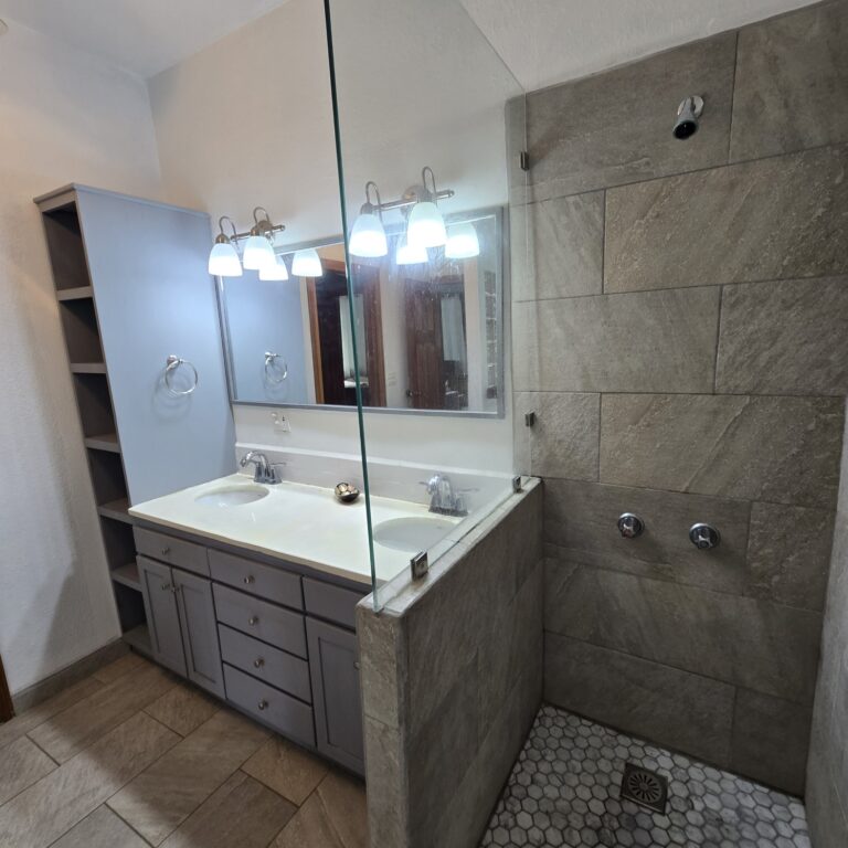 Modern bathroom with dual sinks, large mirror, and a walk-in shower featuring textured stone tiles on Roatan, Honduras.