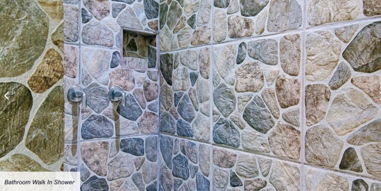 A walk-in shower with walls covered in multicolored natural stone tiles inside a bathroom on Roatan, Honduras, featuring a built-in niche for toiletries and modern chrome shower fixtures.