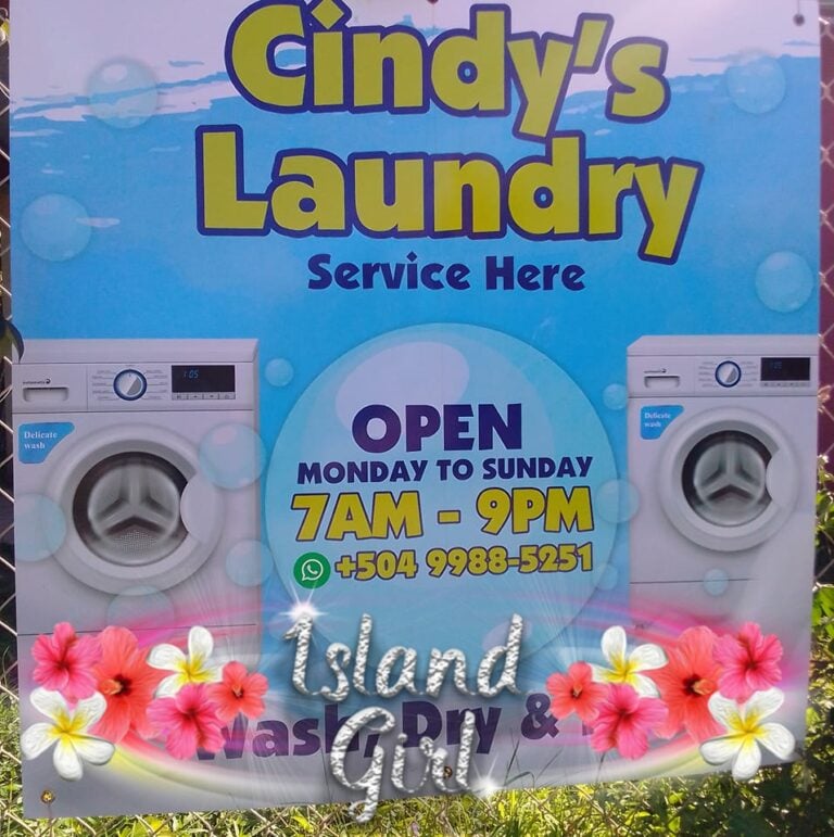 Bright blue sign for Cindy's Laundry in Roatan, Honduras, displaying images of washing machines and details about operating hours from 7 AM to 9 PM Monday to Sunday, with contact information and tropical flower decorations.