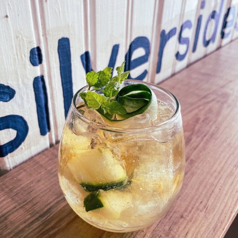 A refreshing cucumber and mint cocktail garnished with a sprig of mint and a slice of cucumber on top, positioned on a wooden surface in Roatan, Honduras.