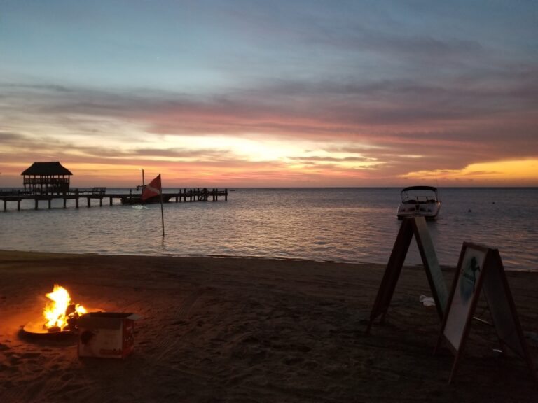 Sunset over Roatan Bay Islands Honduras with a pier, boat, and fire on the beach.