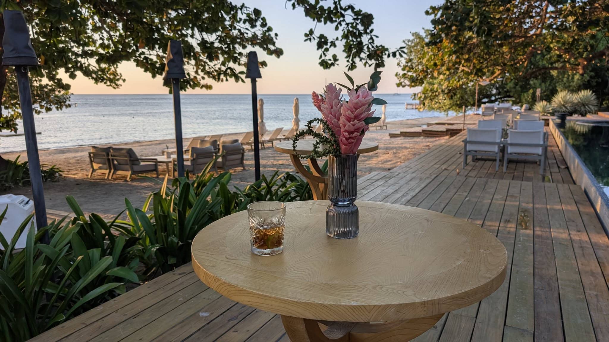 A cozy table with a drink and flowers on a wooden deck by the sea.