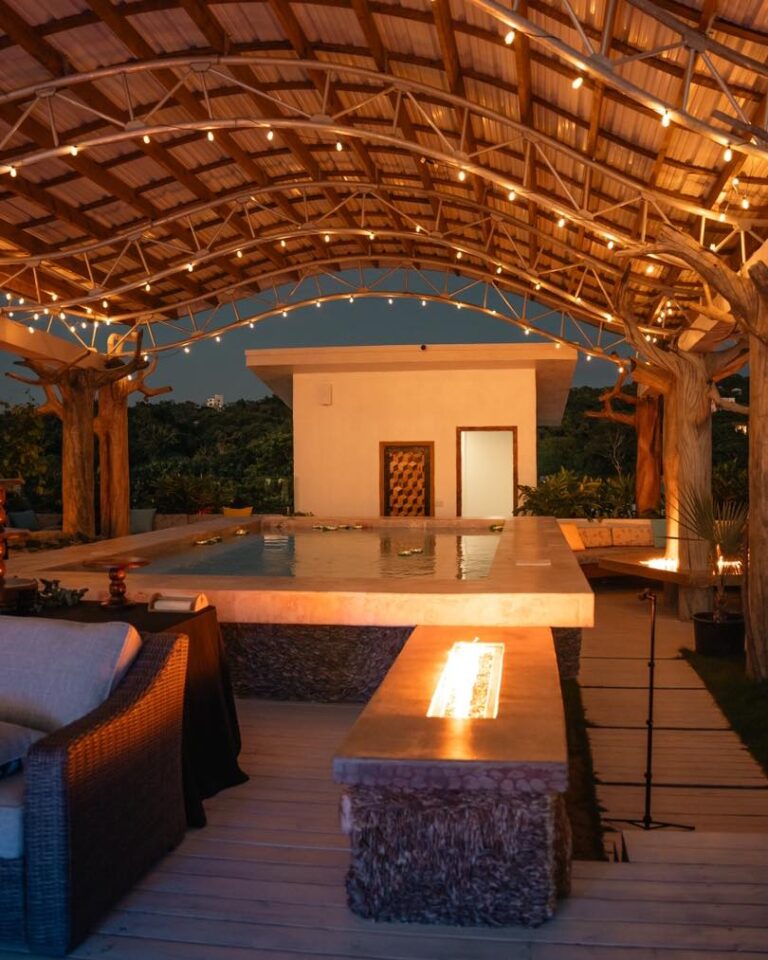 Elegant outdoor lounge area with a hot tub under a wooden canopy adorned with string lights overlooking lush greenery in Roatan, Honduras.