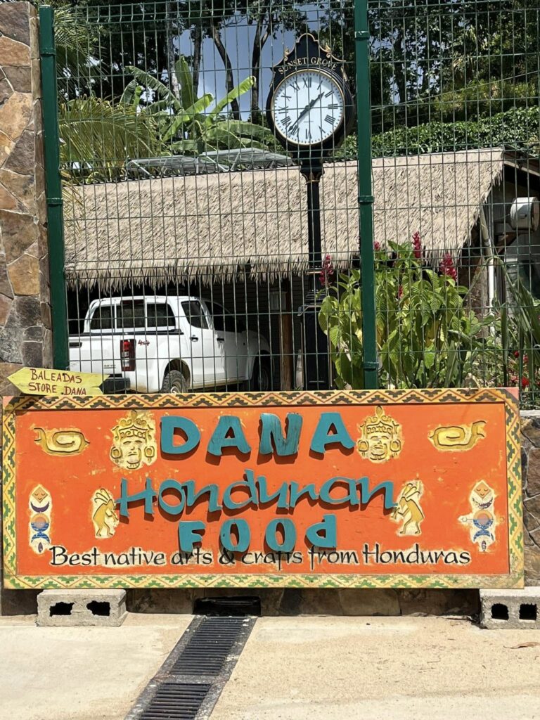 Colorful hand-painted sign advertising Honduran food in Roatan with traditional tribal motifs and bright colors.