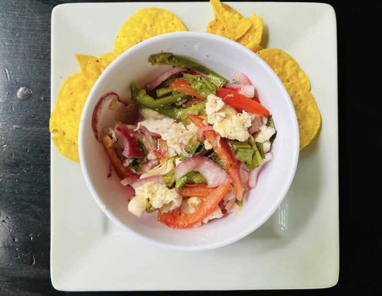 A bowl of fresh ceviche with vegetables and seafood surrounded by yellow tortilla chips on a white plate at a restaurant in Roatan, Honduras.