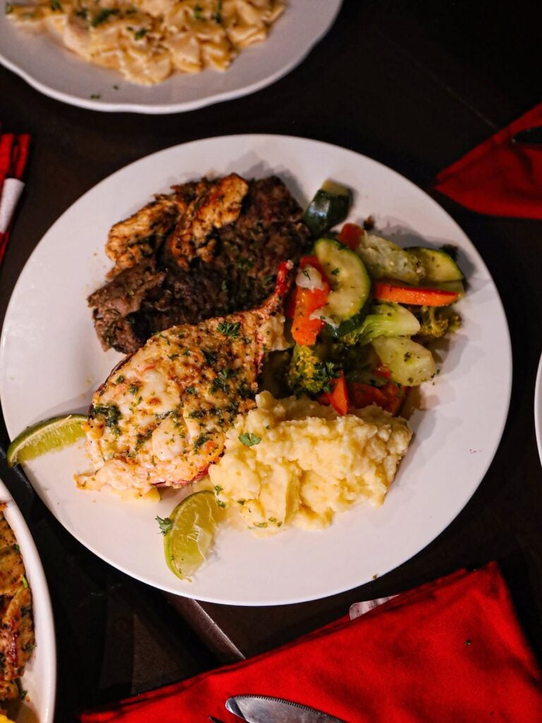 Plate of grilled fish with herb crust, mashed potatoes, and sautéed mixed vegetables on a white dish set on a dark table in Roatan, Honduras.