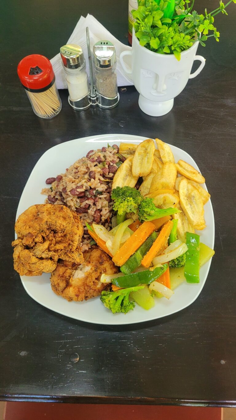 Fried chicken pieces served alongside red beans and rice, and colorful sautéed vegetables on a white plate, with a black table in Roatan, Honduras.
