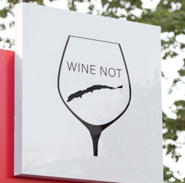 A white sign with a black outline of a wine glass displaying the message 'WINE NOT' and a stylized map of Roatan in Honduras inside the glass.