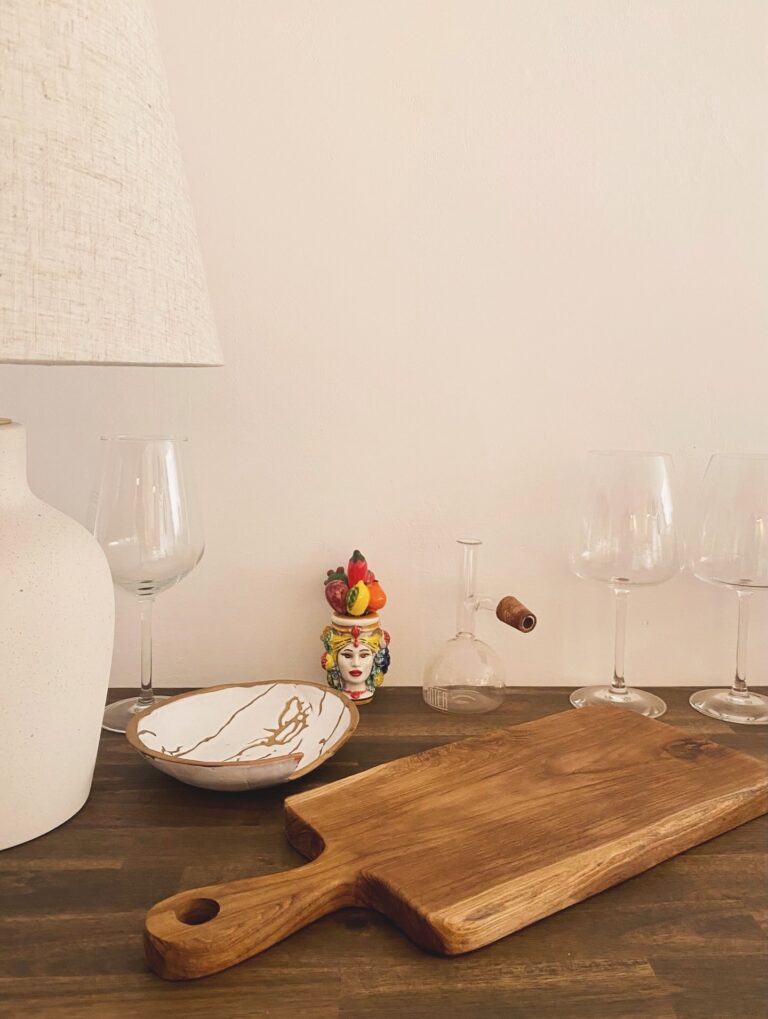 Display of glassware and decorative items on a wooden table against a plain white wall in Roatan, Honduras.
