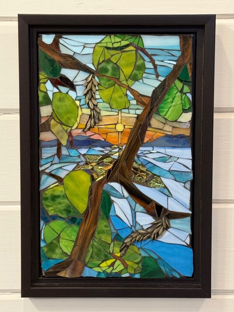 Colorful stained glass window depicting a tropical scene with green leaves, brown branches, and a sunset over water near Roatan and Honduras.