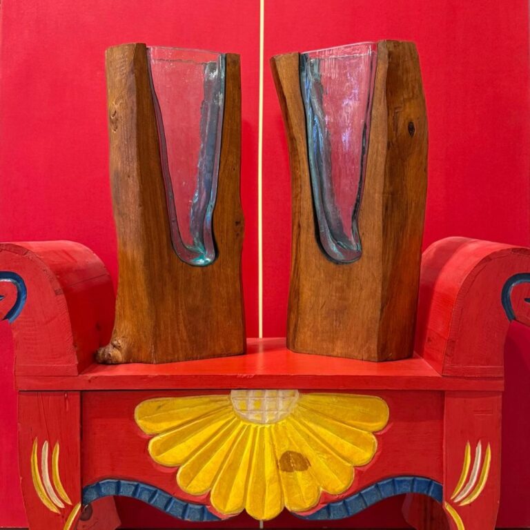 Two handcrafted wooden and glass fish sculptures mounted on a colorful painted wooden table against a red wall in Roatan, Honduras.