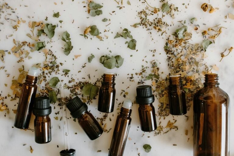 Glass bottles with essential oils surrounded by dried leaves and herbs on a white surface in Roatan, Honduras.