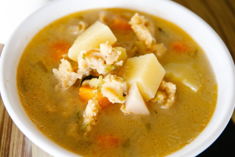 A bowl of traditional Honduran sopa de mondongo featuring tripe, potatoes, carrots, and vegetables in a flavorful broth, set on a wooden surface with a blurred background.