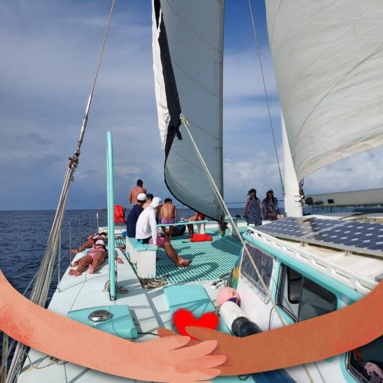 Group of people relaxing and sailing on a catamaran off the coast of Roatan in Bay Islands, Honduras, with a clear sky and calm ocean waters.