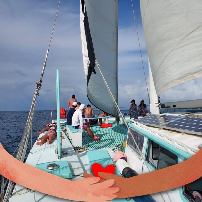 People relaxing and sailing on a sailboat near Roatan, Bay Islands, Honduras with a clear blue sky overhead.