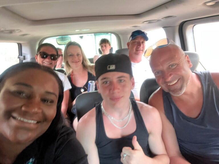 A group of smiling people taking a selfie inside a vehicle on Roatan, Bay Islands, Honduras during a sunny day.
