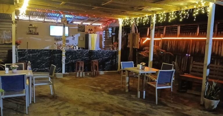 Cozy open-air bar with string lights, wooden tables, and a marble-topped counter on Roatan, Honduras.