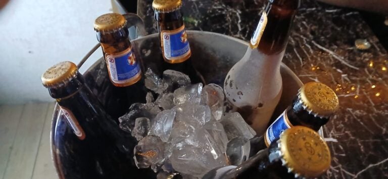 Six bottles of imported beer chilling in a bucket filled with ice on a dark marble countertop in Roatan, Honduras.