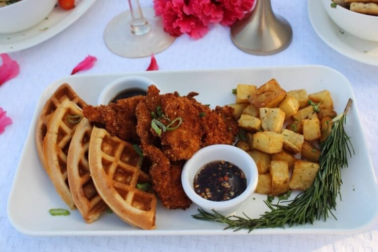 Crispy fried chicken with waffles, roasted potatoes, and dipping sauces served on a white plate at a restaurant in Roatan, Honduras.