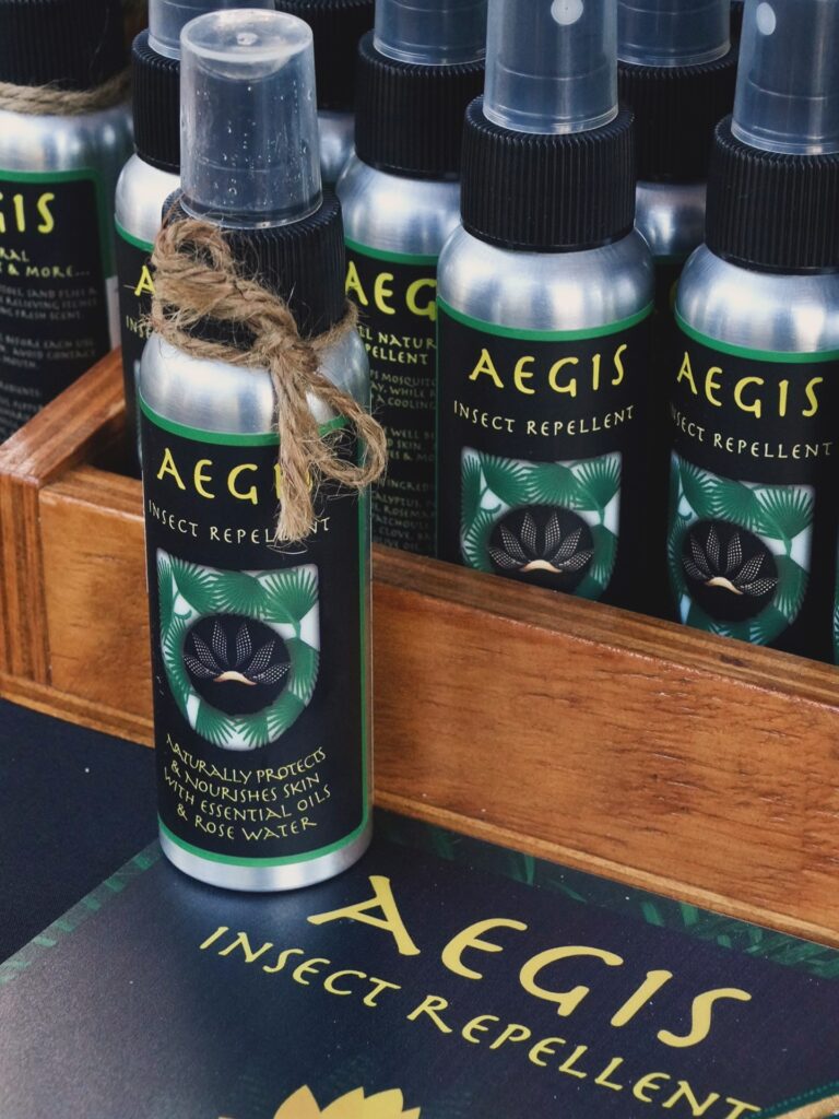 Small aluminum bottles of Aegis insect repellent with tropical leaf and flower island-themed labels on a wooden display box on a Roatan, Honduras business website.