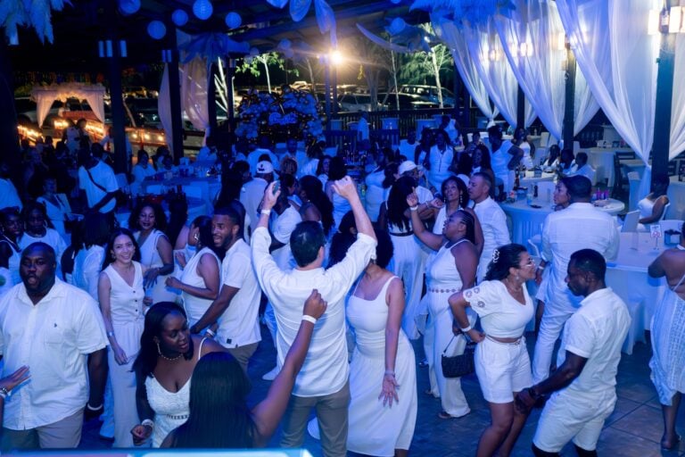 A lively nighttime celebration on Roatan featuring a large group of people dancing under white drapery and decorated lights with a stage in the background of the venue in Honduras.