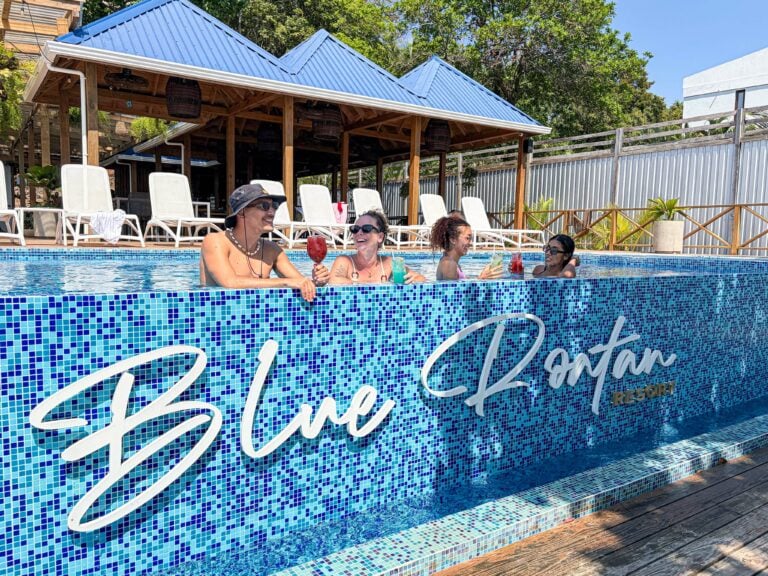 People enjoying a poolside bar at a beachfront resort in Roatan, Honduras, with a thatched-roof structure and lounge chairs in the background.