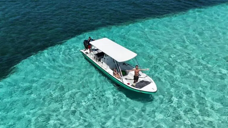 Three people enjoying a boat cruise in the clear turquoise waters near Roatan, Honduras, with a lush island shoreline visible in the distance.