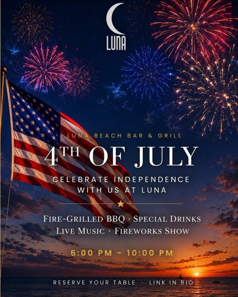 Fireworks explode in the night sky over Roatan, Honduras, with an American flag waving in the foreground during a 4th of July celebration at Luna Beach Bar & Grill.