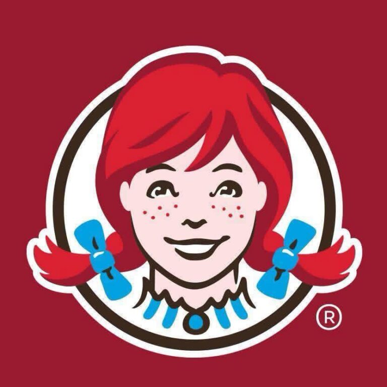 A cartoon illustration of Ronald McDonald with red hair, rosy cheeks, and a big smile, wearing a yellow and red costume with blue accessories, set against a red background representing McDonald's branding in Roatan, Honduras.