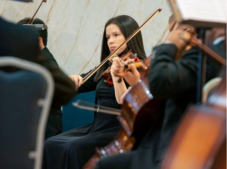 A young woman playing the violin during a classical music performance at a venue in Roatan, Honduras, with fellow musicians nearby.