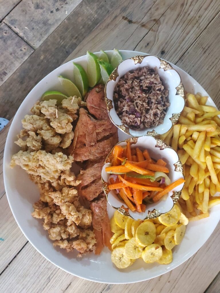 A plate of traditional Honduran food served on a wooden table in Roatan, Bay Islands, featuring rice, fried fish, fried plantains, seasoned vegetables, and lime wedges.