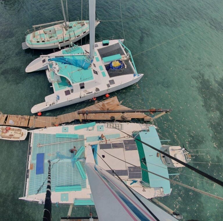 Aerial view of two modern sailing yachts docked at a wooden pier in Roatan, Honduras, with turquoise waters surrounding them.