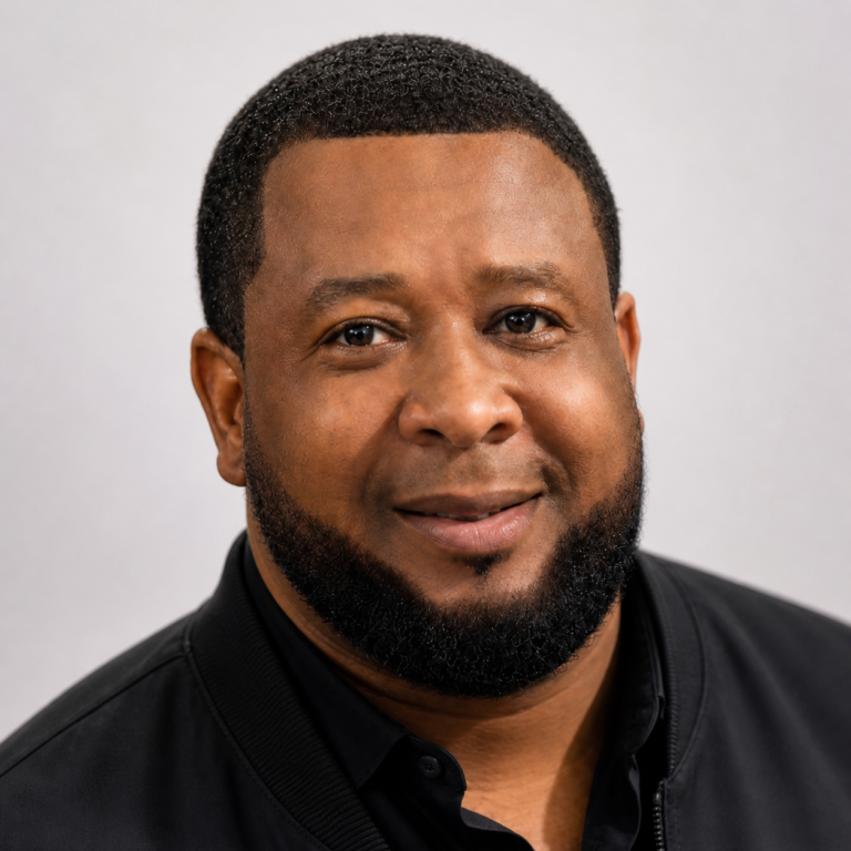 Close-up portrait of a smiling African American man with short black hair and a beard, wearing a black shirt against a neutral background in Roatan, Honduras.