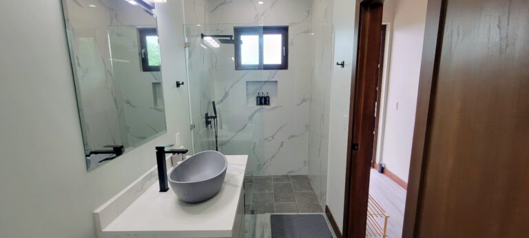 Modern bathroom with white marble walls and a walk-in shower featuring black fixtures and a small window in Roatan, Honduras.