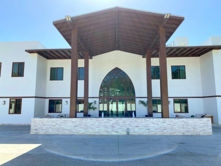 Modern white building on Roatan with a large wooden pergola-style roof structure and glass doors, set against a clear blue sky in Honduras.