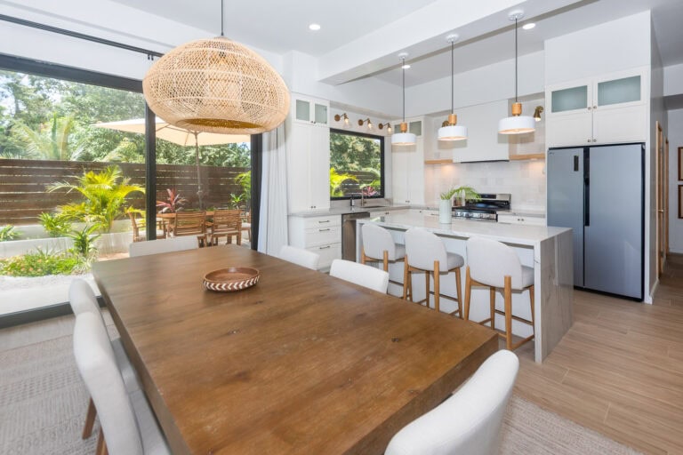 Modern kitchen and dining area with large sliding glass doors opening to a tropical garden on Roatan, Honduras, showcasing a bright and airy interior design.