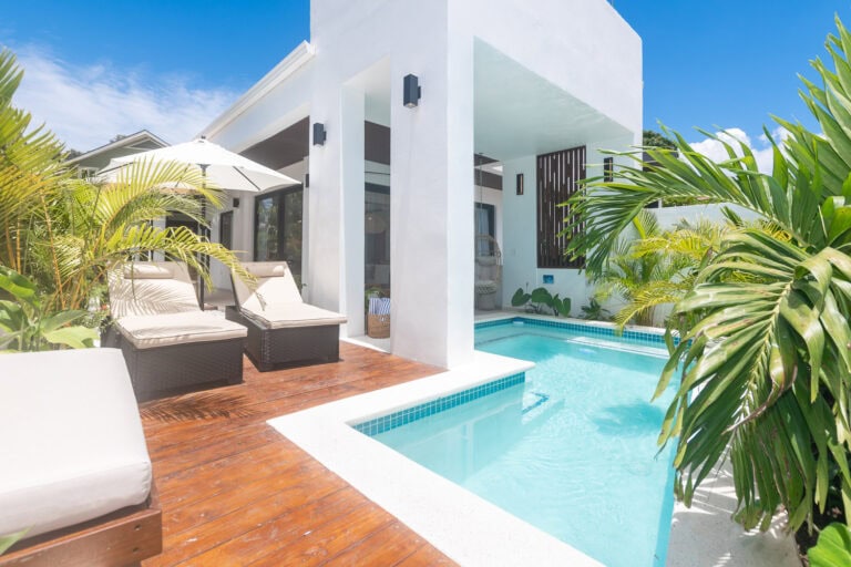 Modern white villa with a private pool surrounded by tropical plants on Roatan, Honduras, under a bright blue sky.