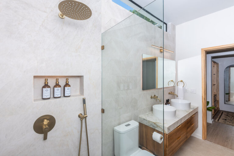 Modern bathroom with dual vessel sinks, gold fixtures, a frameless glass shower, and a skylight in Roatan, Honduras.